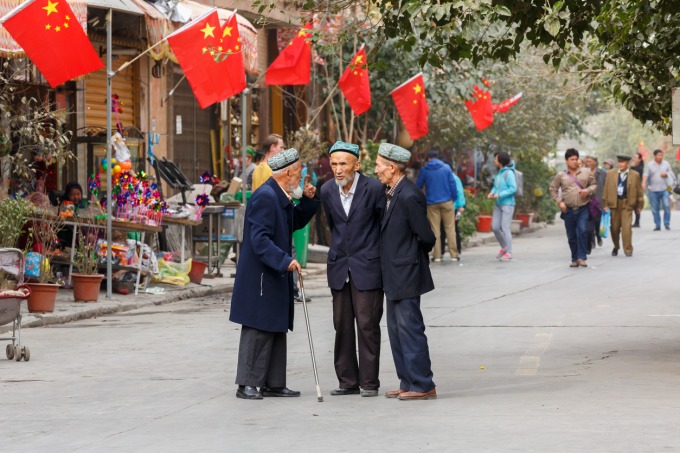 （写真）新疆ウイグル自治区のカシュガルで話すウイグル人の老人。ただし背景には中国の国旗である五星紅旗がはためく。（2017年、iStock）